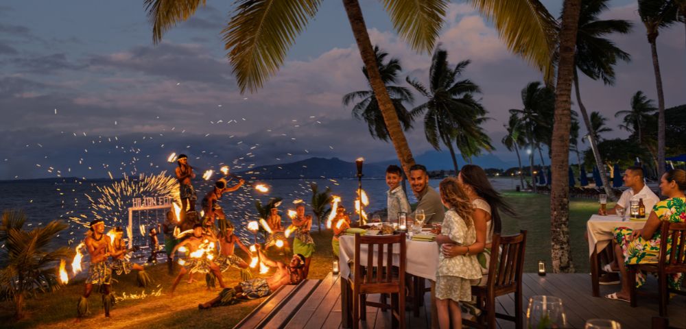 Outdoor dining setup with tables and chairs overlooking the ocean at sunset.