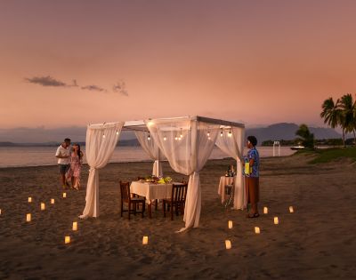 Romantic beachfront dining table with white canopy and sunset view.