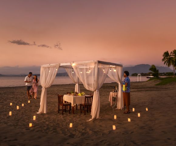 Romantic beachfront dining table with white canopy and sunset view.