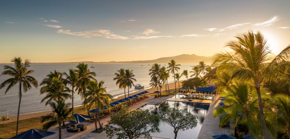 Drone view of a beachfront resort with palm trees and ocean.