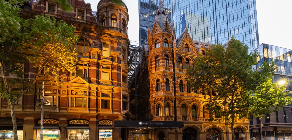 Evening view of InterContinental Melbourne The Rialto’s illuminated Gothic-style architecture with warm lighting against a dusky sky.