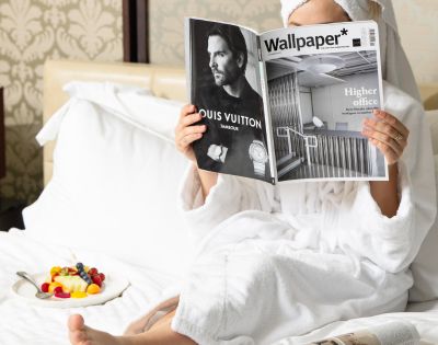 Guest enjoying in-room dining at InterContinental Melbourne The Rialto with breakfast tray and magazine on a white bed.