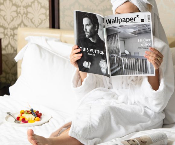 Guest enjoying in-room dining at InterContinental Melbourne The Rialto with breakfast tray and magazine on a white bed.
