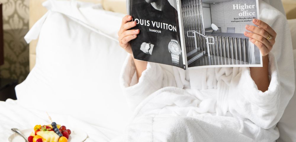 Guest enjoying in-room dining at InterContinental Melbourne The Rialto with breakfast tray and magazine on a white bed.