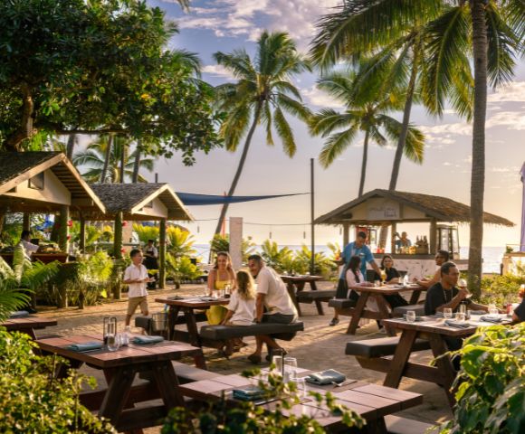 Beachfront dining setup with tables under palm trees and string lights at DoubleTree Resort by Hilton Hotel Fiji.