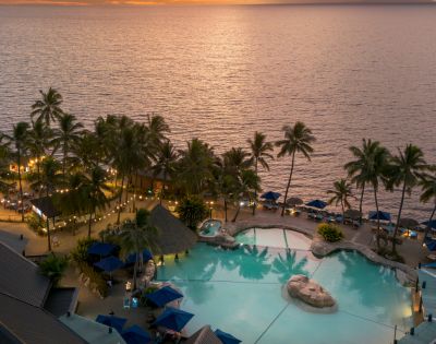 Aerial view of a resort pool surrounded by palm trees at sunset, with the ocean in the background at DoubleTree Resort by Hilton Hotel Fiji.