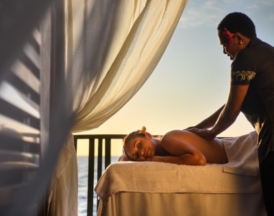 A person receiving an outdoor massage under a white canopy with sheer curtains, overlooking a scenic view at DoubleTree Resort by Hilton Hotel Fiji.