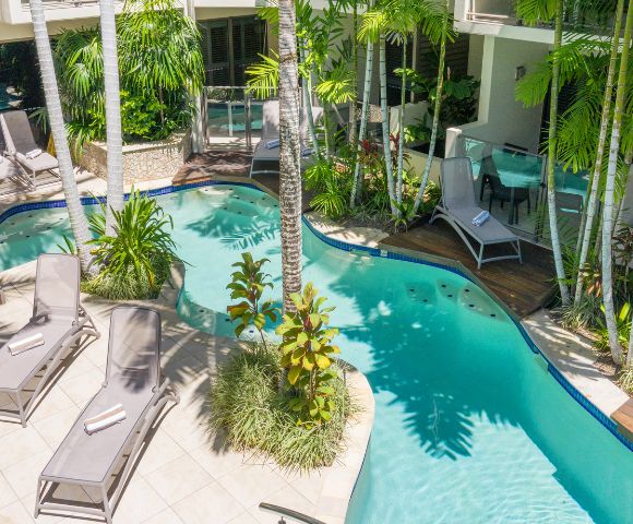 Swimming pool surrounded by palm trees and sun loungers in a tropical setting