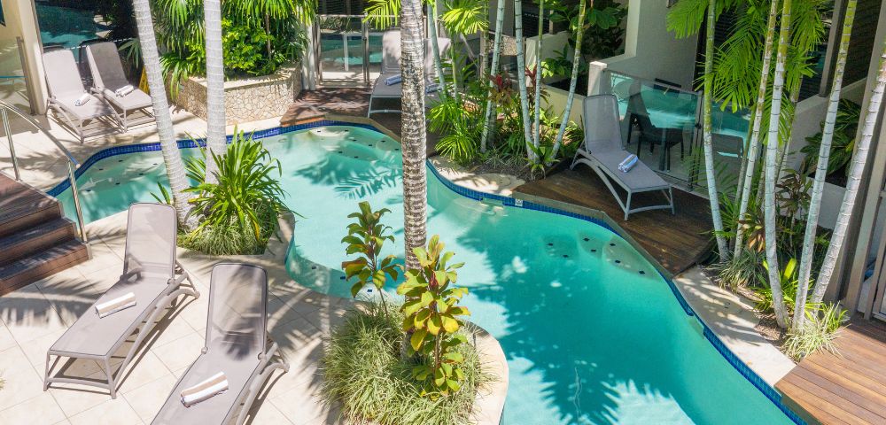 Swimming pool surrounded by palm trees and sun loungers in a tropical setting