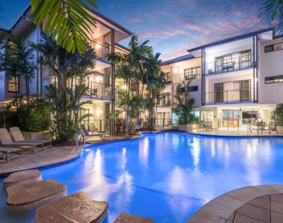 Resort pool at night with illuminated water and reflections of palm trees.