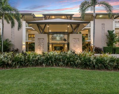 Elegant resort entrance framed by palm trees at sunset, with lush greenery and a welcoming, luxurious ambiance. Sky features vibrant pink and purple hues.