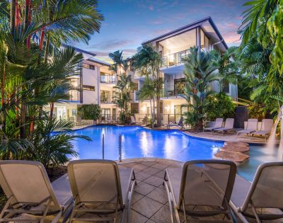 Resort pool at night with illuminated water and reflections of palm trees.