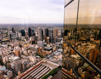 Aerial view of a bustling city skyline with modern skyscrapers. The glass facade of a nearby building reflects the urban landscape, creating a dynamic scene.