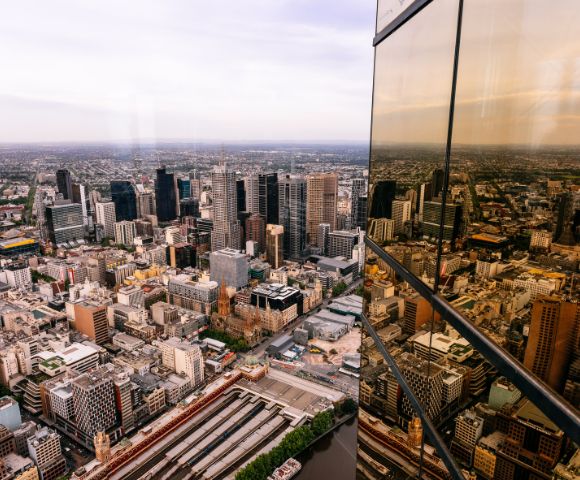 Aerial view of a bustling city skyline with modern skyscrapers. The glass facade of a nearby building reflects the urban landscape, creating a dynamic scene.