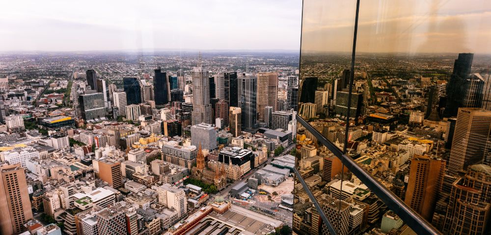 Aerial view of a bustling city skyline with modern skyscrapers. The glass facade of a nearby building reflects the urban landscape, creating a dynamic scene.