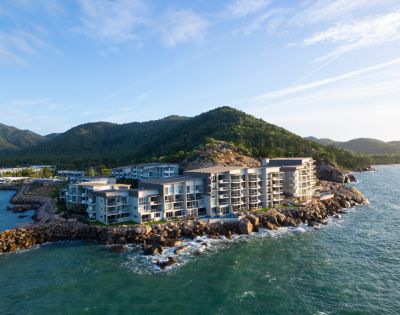 Modern seaside resort on rocky coastline, surrounded by lush green hills and calm ocean waves. Bright, clear day with a serene atmosphere.