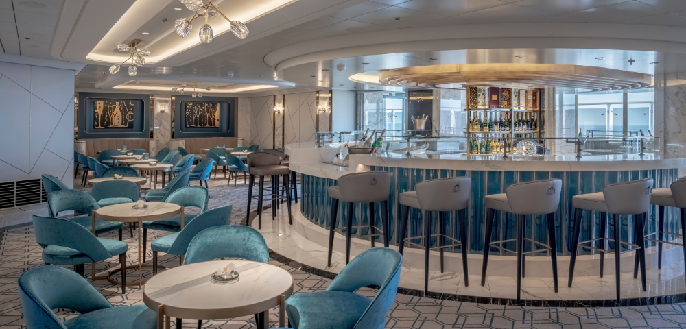 Chic bar area featuring elegant blue chairs, round tables, and a modern, well-stocked bar illuminated by stylish lighting.