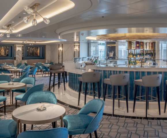 Chic bar area featuring elegant blue chairs, round tables, and a modern, well-stocked bar illuminated by stylish lighting.