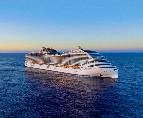 A large, modern cruise ship sails on calm open water under a clear sky at sunset.