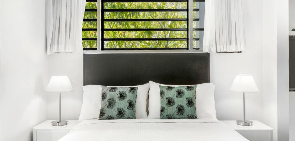 Bright, minimalist bathroom with a large mirror reflecting a modern sink, chrome faucet, and white towels. The atmosphere is clean and serene.
