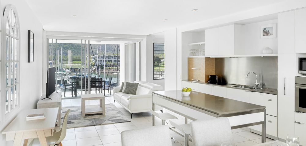 Modern interior featuring a bright bedroom and adjacent bathroom. Bedroom has a cozy bed, lamp, and artwork; bathroom includes a sleek vanity and round tub. Airy and serene ambiance.