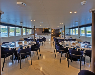 A room featuring multiple tables and chairs arranged for dining, with a ceiling overhead and a floor underneath. The space is designed for social gatherings, resembling a cafeteria or restaurant setting.