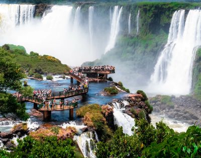 A majestic waterfall cascading into a rocky basin with thick jungle vegetation around it. Water spray creates a misty effect, adding drama to the scene.