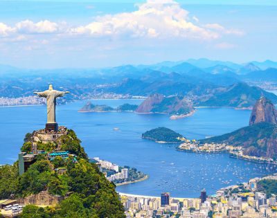 The iconic Christ the Redeemer statue overlooking Rio de Janeiro with the city and ocean below. Blue waters and scattered islands enhance the panoramic view.