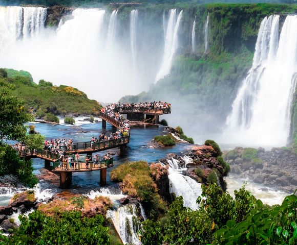 A majestic waterfall cascading into a rocky basin with thick jungle vegetation around it. Water spray creates a misty effect, adding drama to the scene.