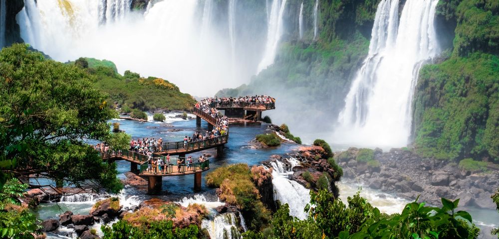 A majestic waterfall cascading into a rocky basin with thick jungle vegetation around it. Water spray creates a misty effect, adding drama to the scene.