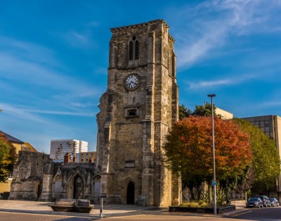 Historic stone church tower with a clock under a clear blue sky, surrounded by trees with autumn foliage. The scene evokes a calm, timeless feel.