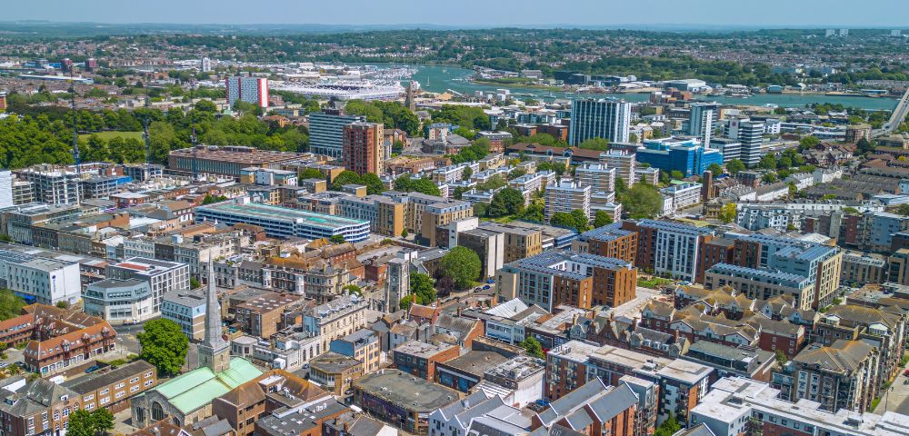 Aerial view of a cityscape on a clear day, featuring densely packed buildings of various heights and architectural styles, surrounded by green spaces.