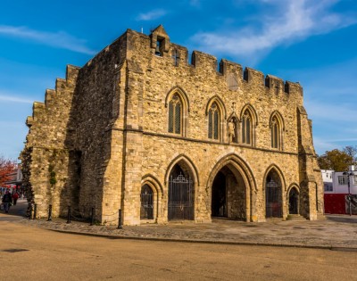 A historic, medieval stone building with arched entrances and a crenellated roof under a clear blue sky, conveying a sense of timelessness.