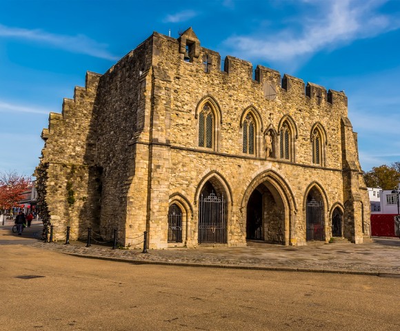 A historic, medieval stone building with arched entrances and a crenellated roof under a clear blue sky, conveying a sense of timelessness.