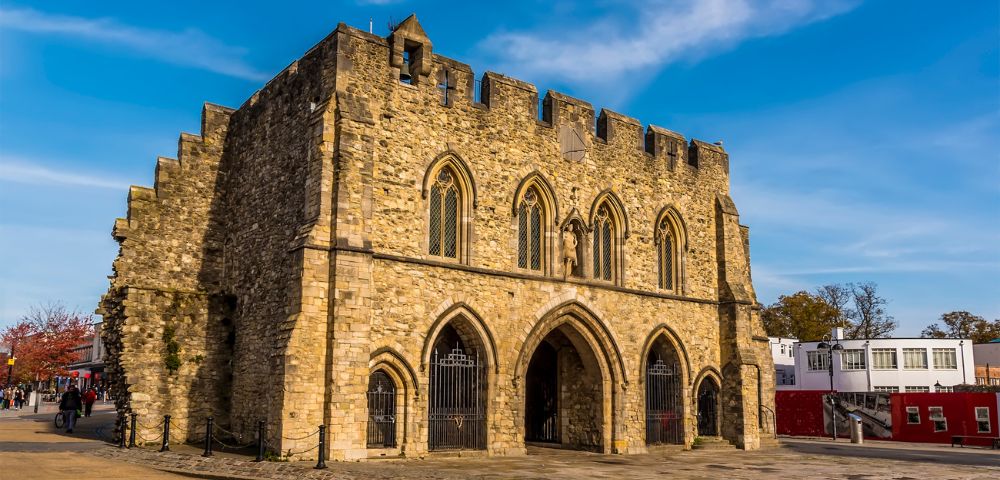 A historic, medieval stone building with arched entrances and a crenellated roof under a clear blue sky, conveying a sense of timelessness.