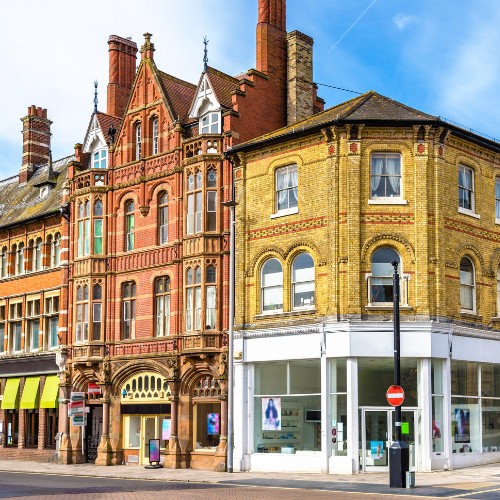 Historic street corner featuring colorful Victorian buildings with ornate brickwork and large arched windows, set against a blue sky.