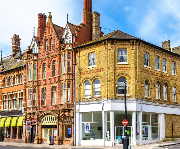 Historic street corner featuring colorful Victorian buildings with ornate brickwork and large arched windows, set against a blue sky.