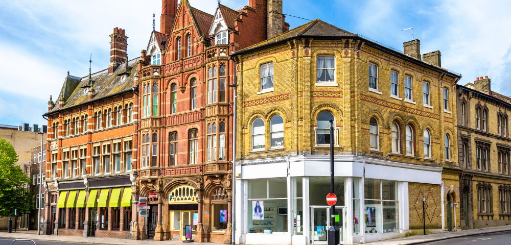 Historic street corner featuring colorful Victorian buildings with ornate brickwork and large arched windows, set against a blue sky.