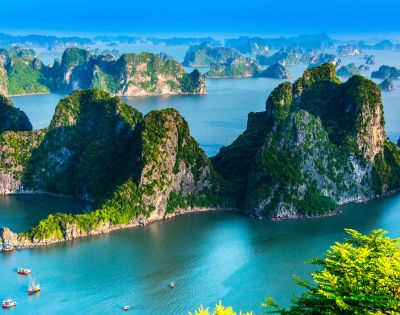 Scenic view of Ha Long Bay, Vietnam, with towering limestone islands covered in green foliage, surrounded by tranquil blue water under a clear sky.
