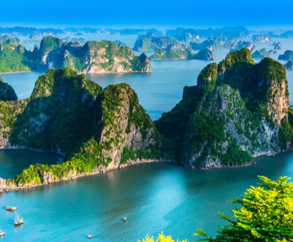 Scenic view of Ha Long Bay, Vietnam, with towering limestone islands covered in green foliage, surrounded by tranquil blue water under a clear sky.