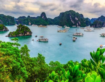 Scenic view of Ha Long Bay with emerald waters, lush green islands, and boats gently sailing beneath a cloudy sky, conveying tranquility and natural beauty.