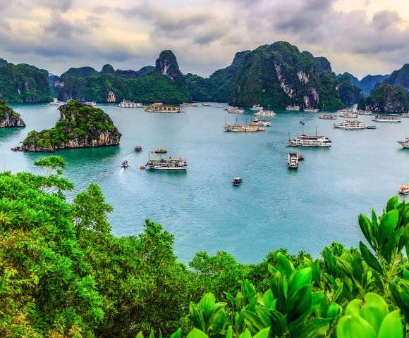 Scenic view of Ha Long Bay with emerald waters, lush green islands, and boats gently sailing beneath a cloudy sky, conveying tranquility and natural beauty.