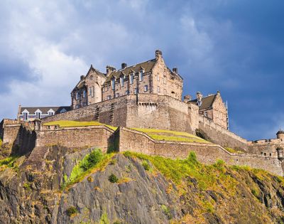 A majestic medieval castle perched on a rocky hill, with stone walls and turrets. Sunlit, under a dramatic, cloudy sky, evoking strength and history.
