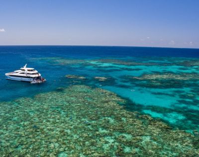 A white yacht is anchored near a vibrant coral reef in clear, turquoise ocean waters under a bright blue sky, conveying a sense of tranquility and adventure.