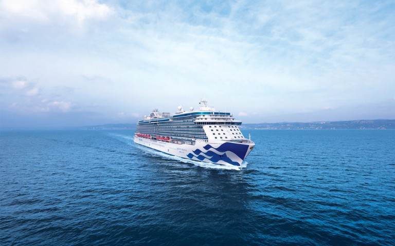A large cruise ship sails across a calm blue ocean under a lightly clouded sky. The ship's design is modern, evoking a sense of adventure and tranquility.
