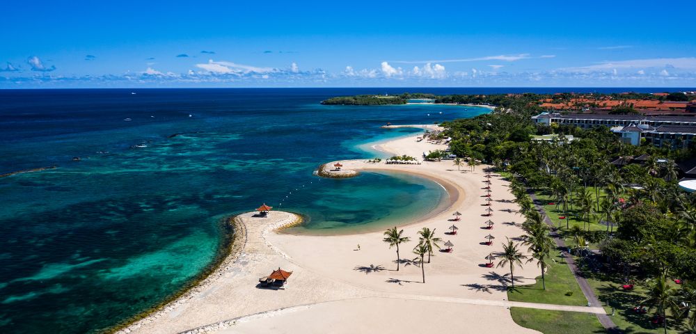 Aerial view of a beautiful Bali beach and resort, showcasing sandy shores and turquoise waters.