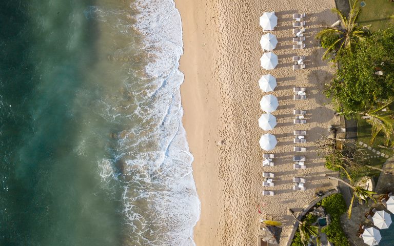 Aerial view of a sunny beach filled with colourful umbrellas and chairs scattered along the sandy shore.