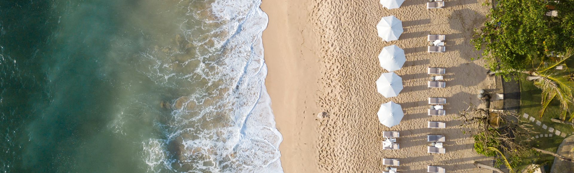 Aerial view of a sunny beach filled with colourful umbrellas and chairs scattered along the sandy shore.