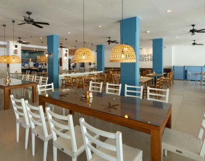 Spacious, modern restaurant interior with wooden tables and white chairs. Woven pendant lights hang from the ceiling, providing a warm, inviting glow.