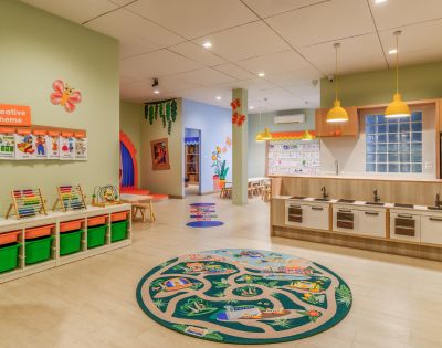 A bright, colorful preschool classroom with a playful, welcoming atmosphere. Features include educational materials, toy kitchen, vibrant decor, and creative-themed displays.
